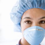 Young female nurse at camera wearing surgical mask